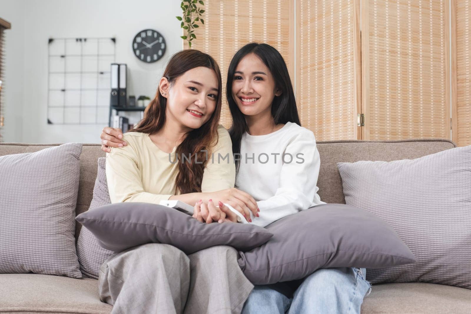 Young LGBT woman, lesbian couple, sitting on the sofa, hugging and smiling happily together in the living room at home. by wichayada