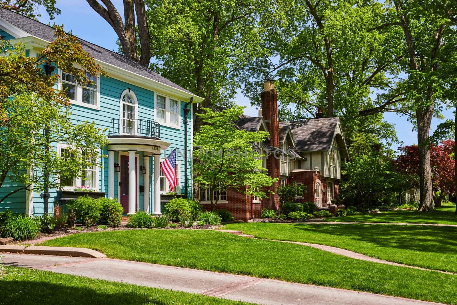 Idyllic suburban street in Fort Wayne, vibrant turquoise home with American flag, and lush greenery.