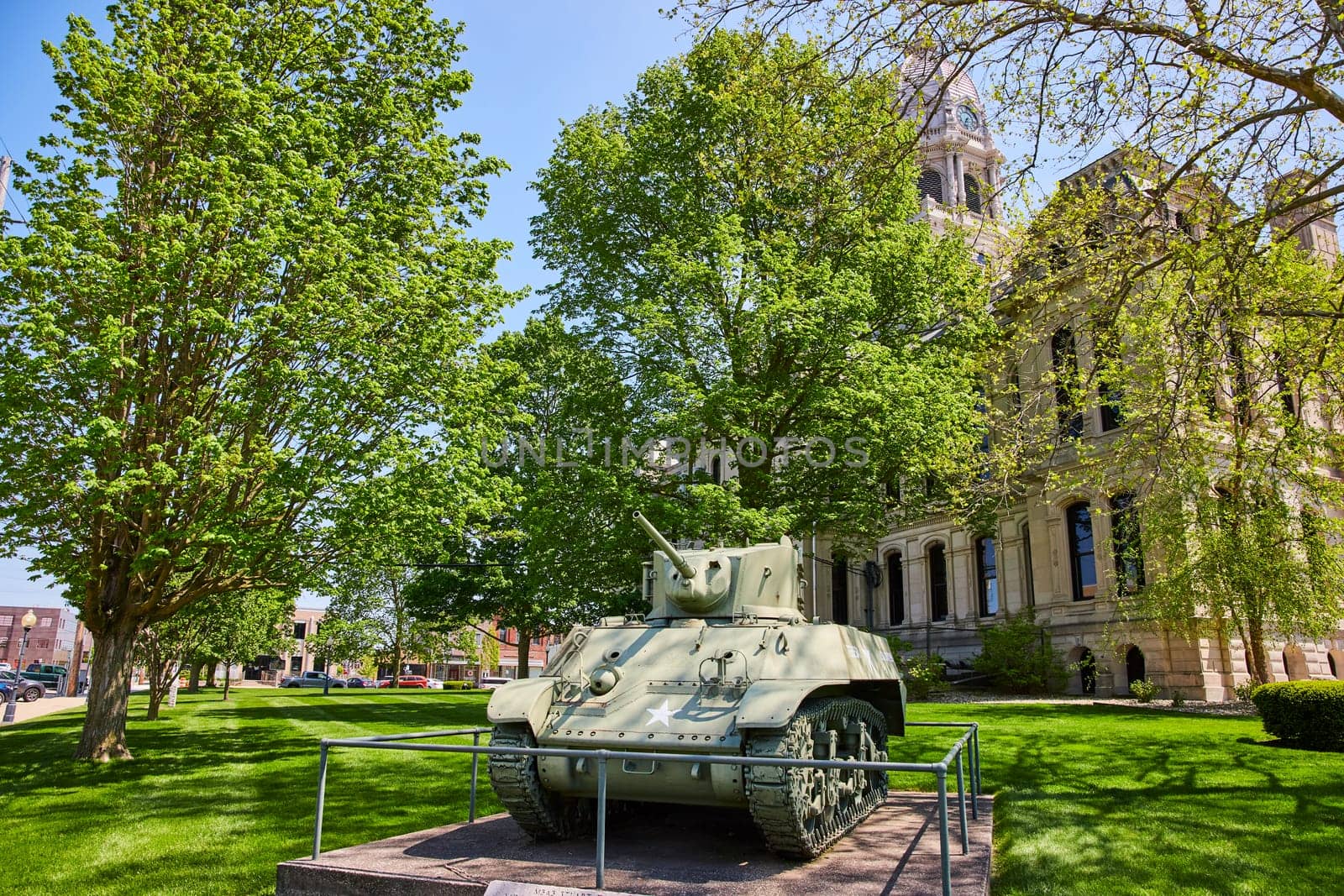Vintage WWII tank on display at Kosciusko County Courthouse, Warsaw, framed by lush greenery.