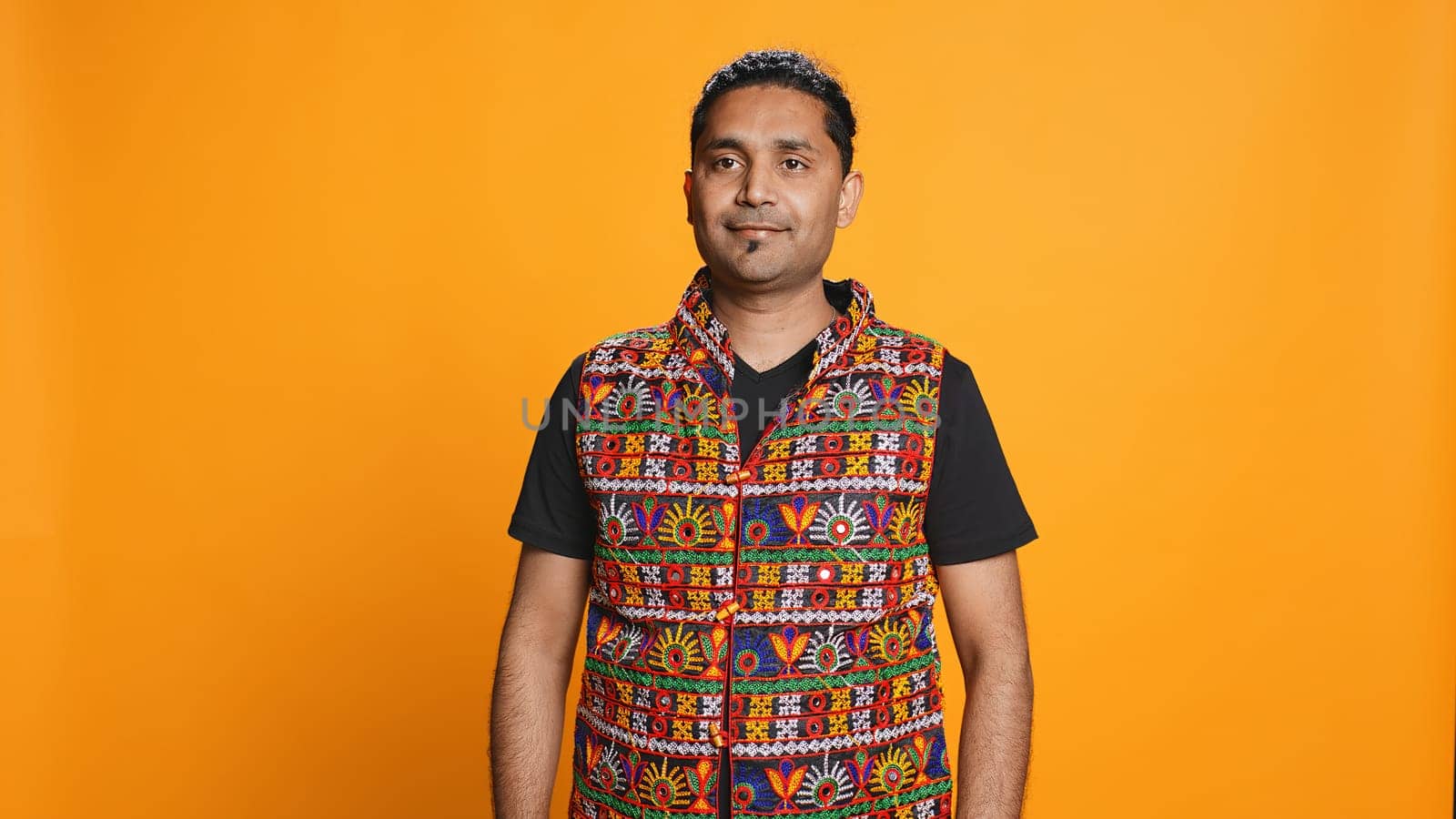 Portrait of cheerful friendly indian man smiling, looking pleased, isolated over studio background. Happy expressive asian person in traditional attire grinning, feeling satisfied, camera B