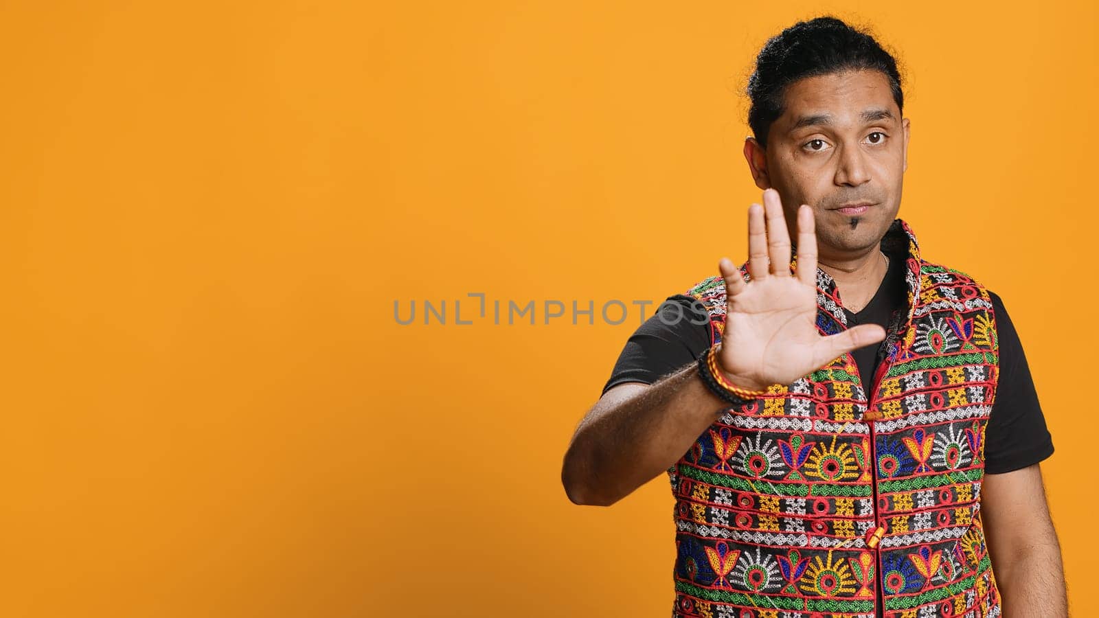 Stern indian man doing stop hand gesture sign, complaining. Authoritative person doing firm halt sign gesturing, wishing to end concept, isolated over studio background, camera A