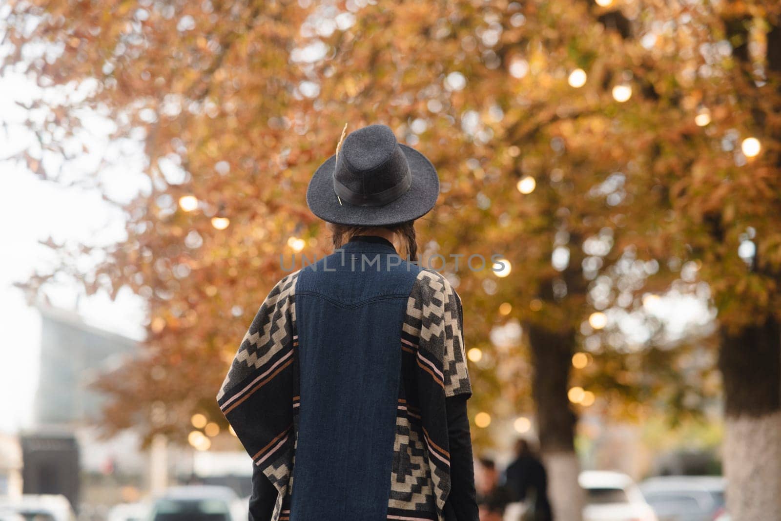 A lovely lady exudes boho chic, adorned with a black hat, amidst the autumnal cityscape. by teksomolika