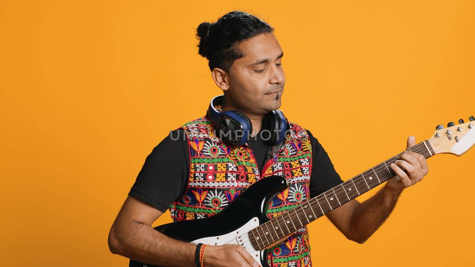 Happy man holding electric guitar, playing rock music, isolated over studio background. Cheerful indian musician using musical instrument, doing concert, playing songs, camera A