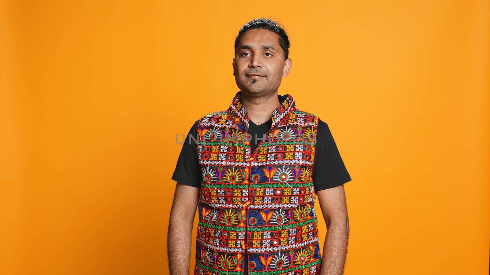 Portrait of jolly indian man with colorful garment smiling, looking pleased, isolated over studio background. Joyous person in traditional attire feeling carefree, camera B