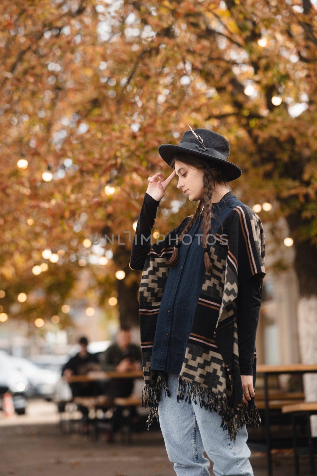 A radiant lady, embracing boho vibes, pairs her look with a black hat while exploring the autumn cityscape. High quality photo