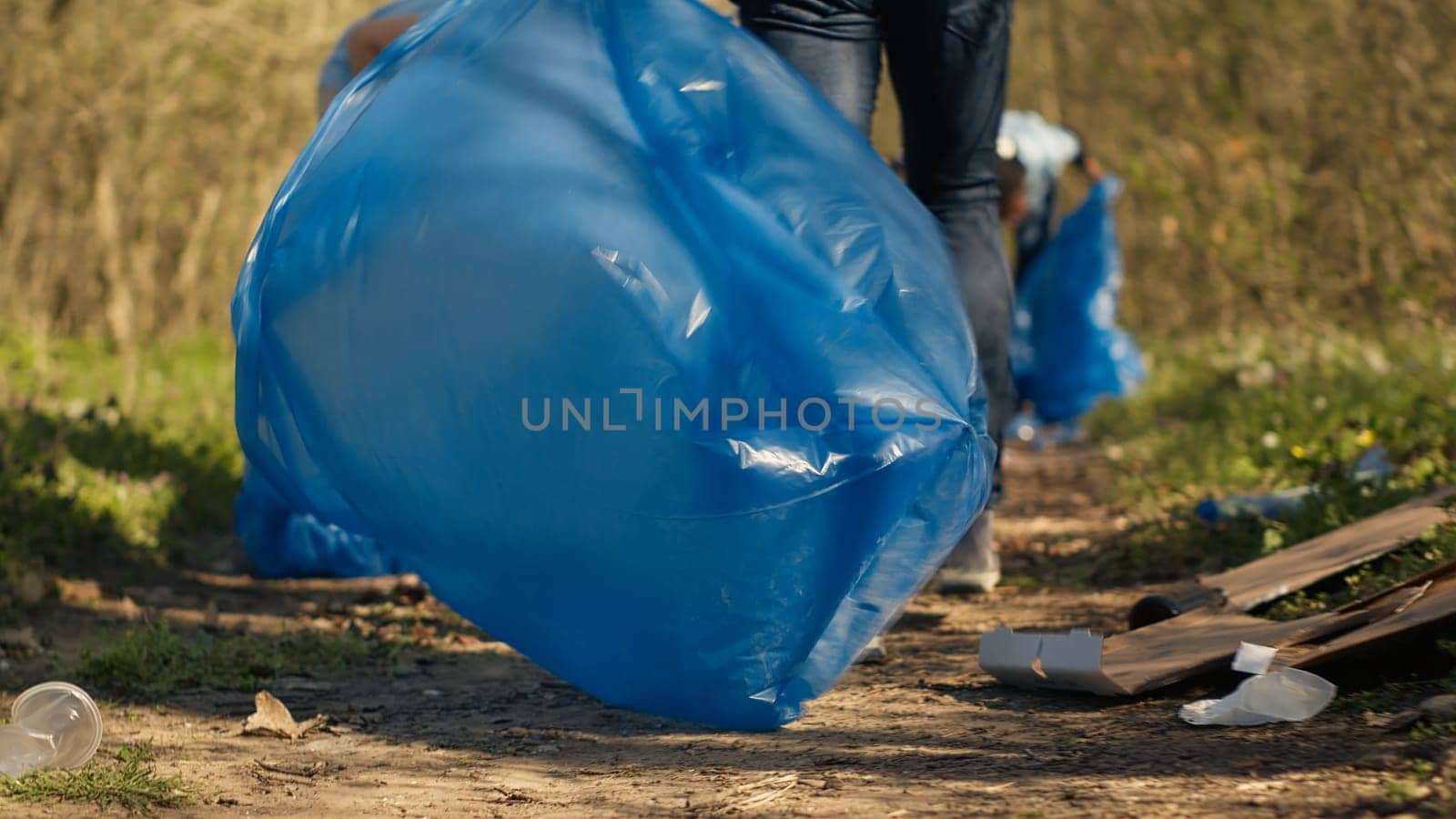 Diverse activists cleaning up rubbish in a garbage disposal bag, environmental conservation concept. Volunteers protecting the forest ecosystem, collecting rubbish with claw tool. Camera A.