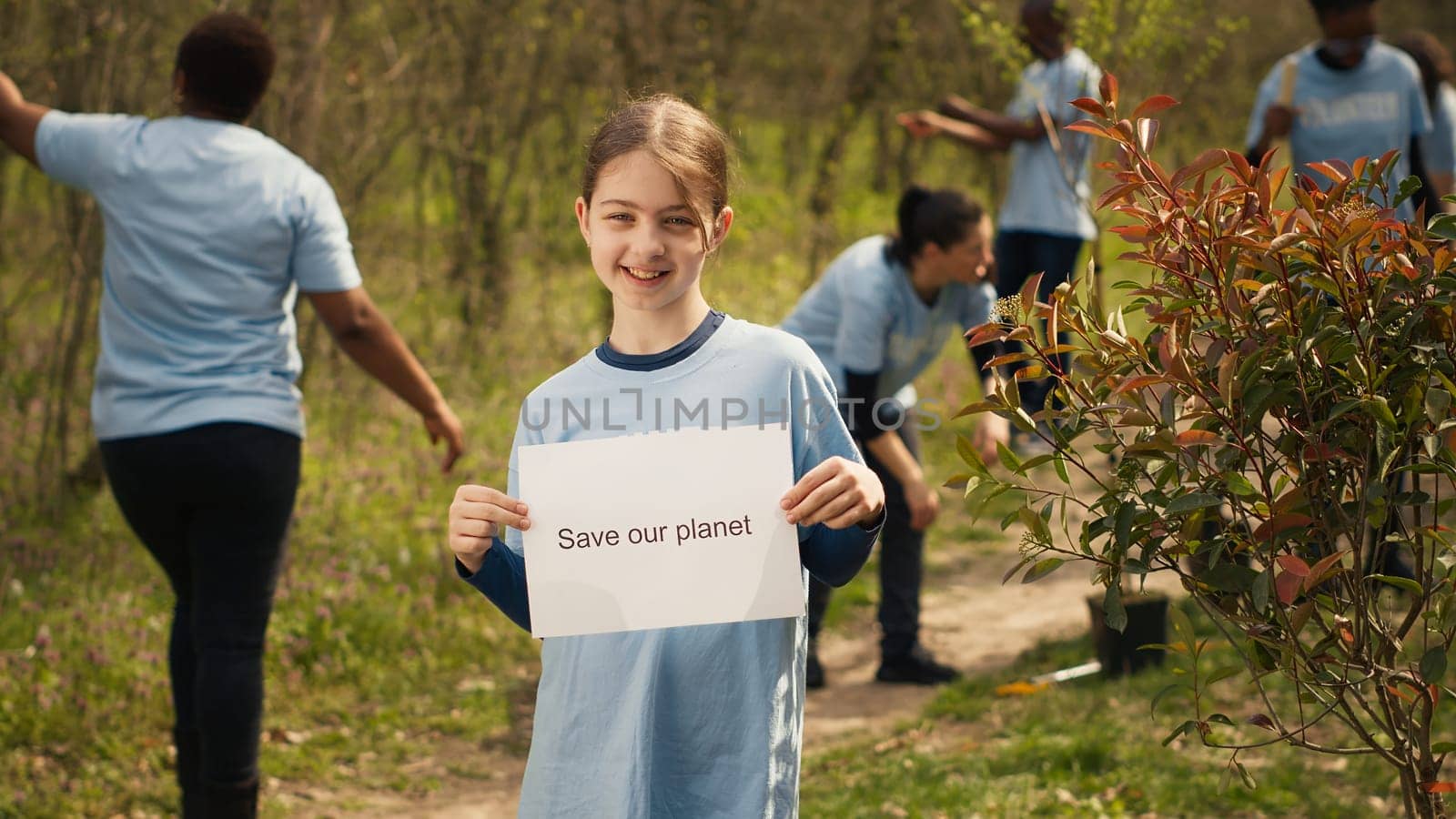 Portrait of sweet girl with save our planet poster against pollution and illegal dumping, volunteering to restore and preserve nature in the forest. Little child shows awareness sign. Camera A.