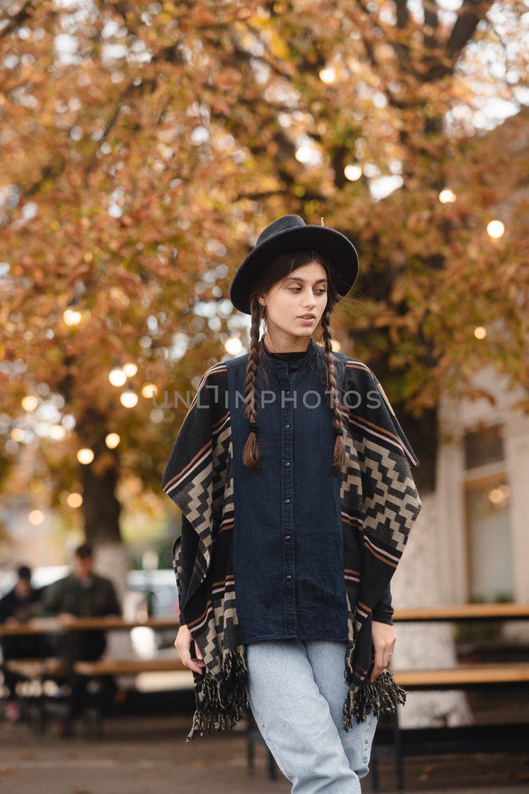 A captivating girl, with bohemian flair, accents her look with a black hat in the fall cityscape. by teksomolika