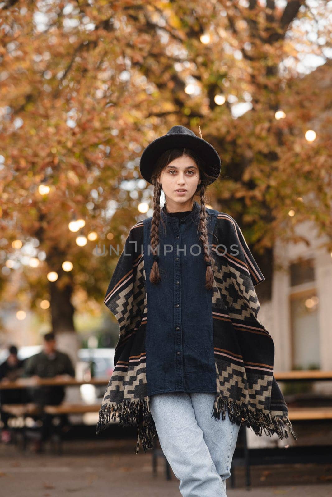 A charming woman, embracing boho fashion, completes her ensemble with a black hat in the autumn city. by teksomolika