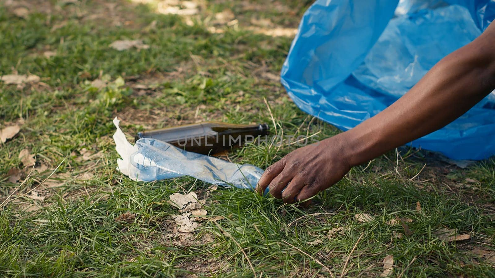 People supporting cleanup of the natural environment by grabbing recyclables and trash objects from the woods, collecting in a garbage bag. Using utensils to pick up rubbish. Close up. Camera A.