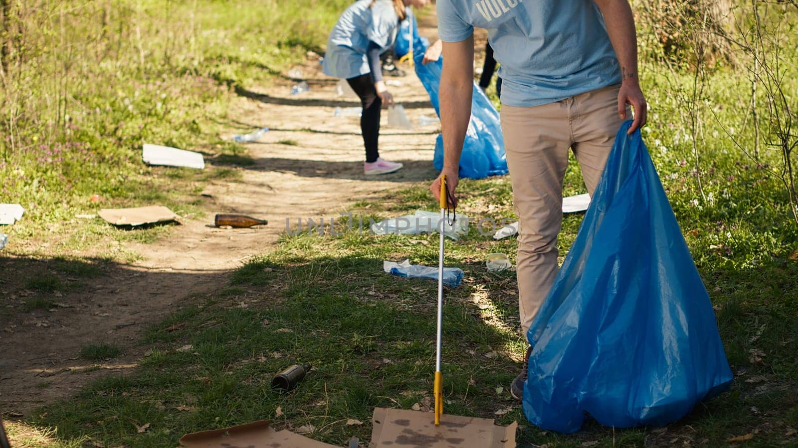 Young volunteer doing litter cleanup with a long claw to grab trash by DCStudio