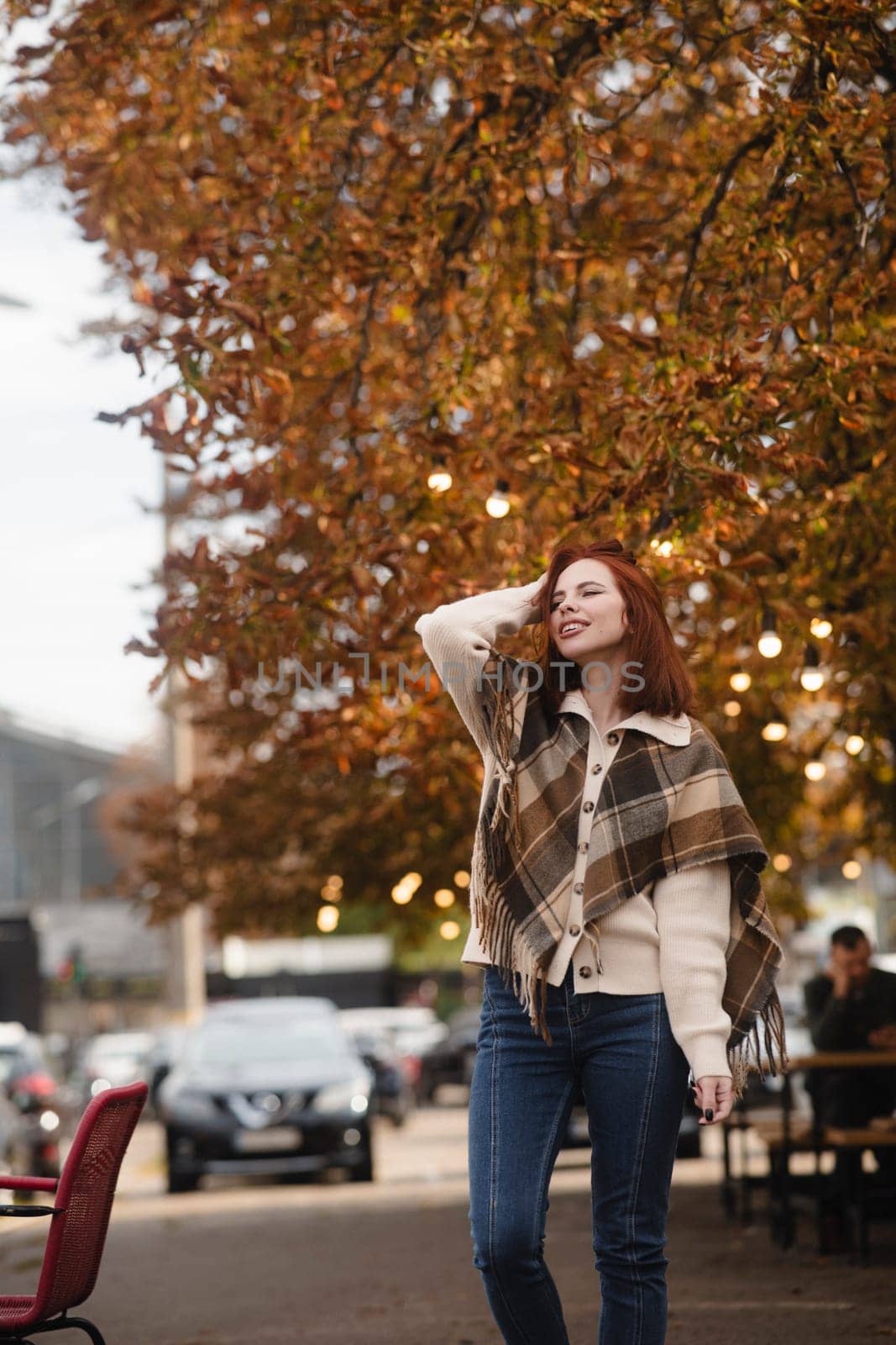 A merry red-haired girl radiates happiness as she walks through the autumn city streets. by teksomolika