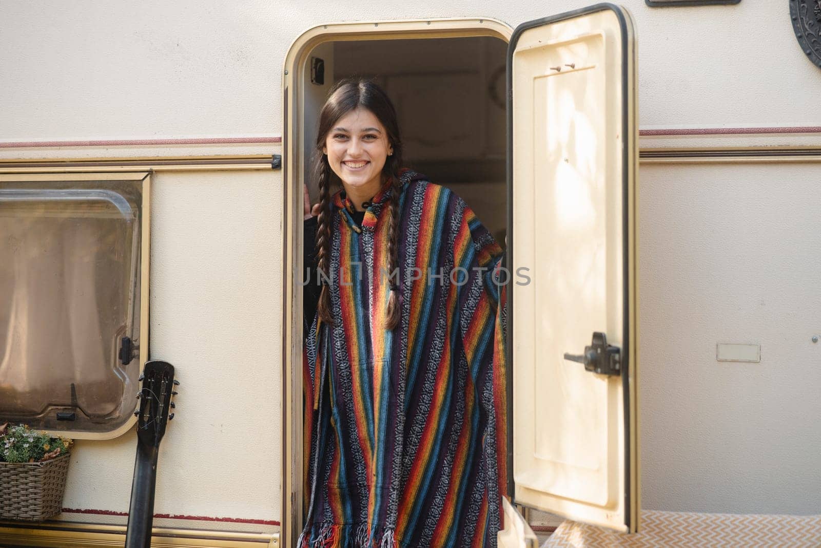 A stunning young woman embraces hippie fashion with a trailer as her backdrop in the park. High quality photo