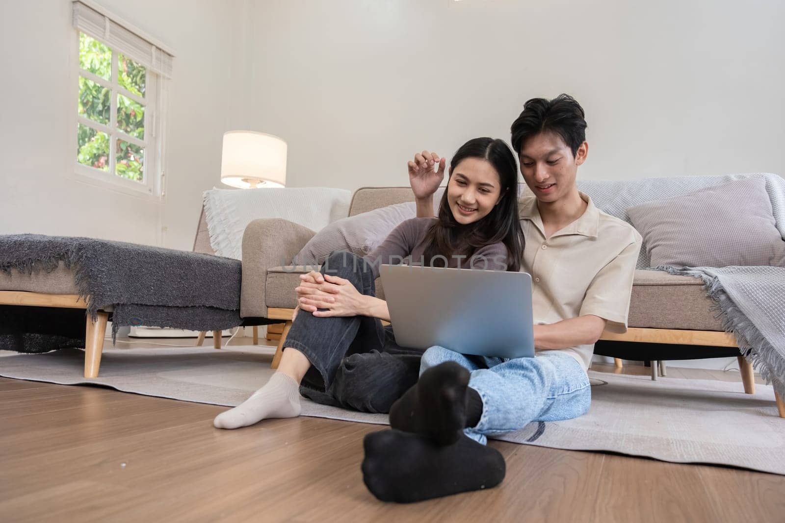 Young Asian couple in love Sitting happily together looking at laptop and relaxing in the living room. Couple making romantic love in the living room.