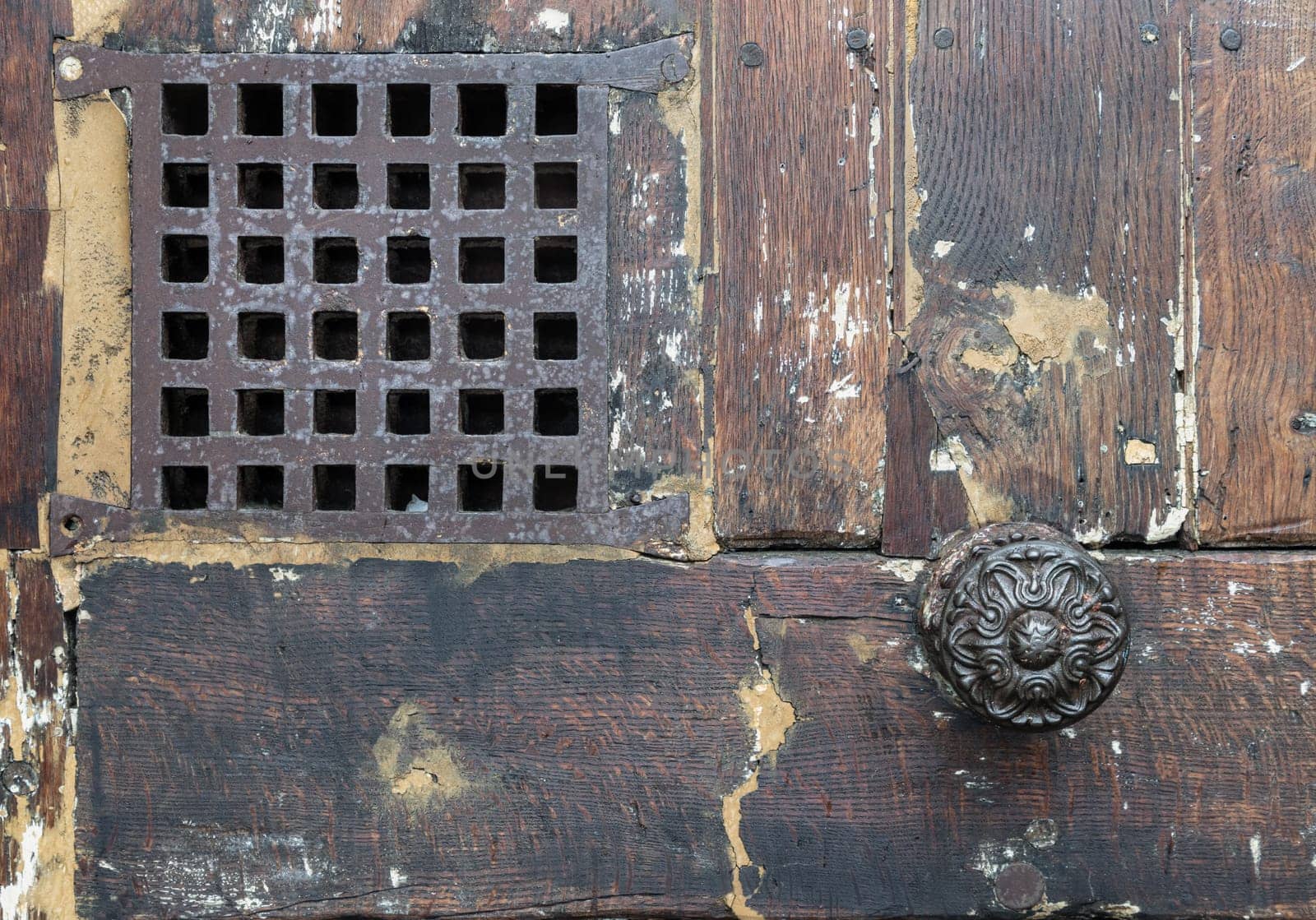 Old medieval door with small peephole. Ancient wooden dark brown door and small window with iron grille, Copy space, Selective focus.