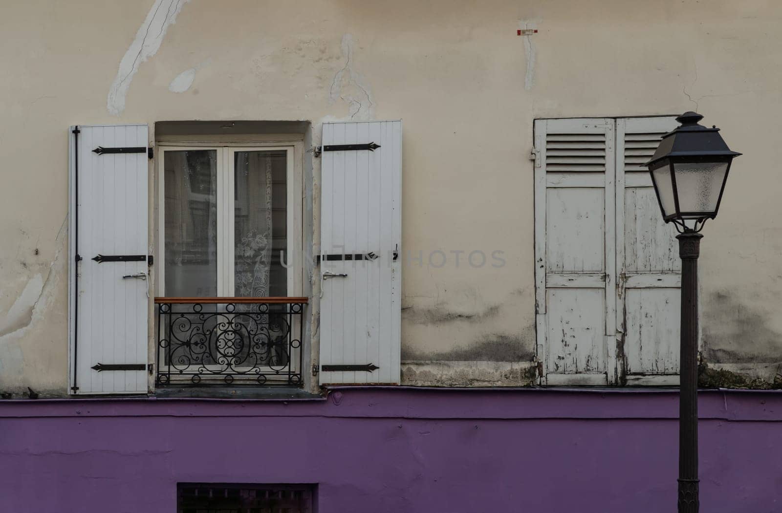 France, Paris - Jan 03, 2024 - Shutters and open window with lace curtained on old wall of a ground floor residence and street lantern. Space for text, Selective focus.
