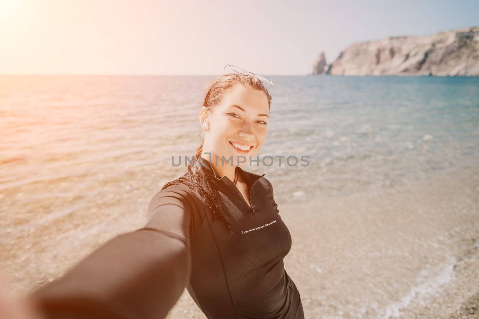 Woman summer travel sea. Happy tourist enjoy taking selfie photo outdoors for memories. Woman traveler posing on the beach at sea surrounded by volcanic mountains, sharing travel adventure journey by panophotograph