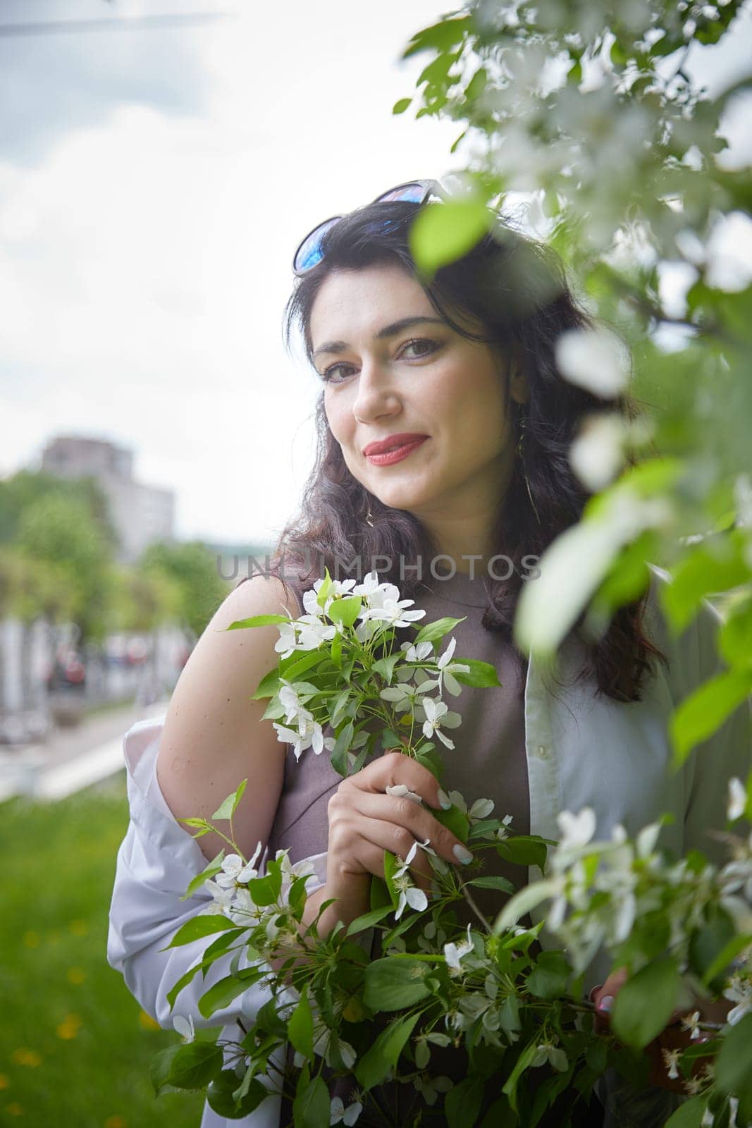 Joyous brunette woman near Blossoms of apple tree in a Spring Garden outdoors. The Concept of face and body care. The scent of perfume and tenderness