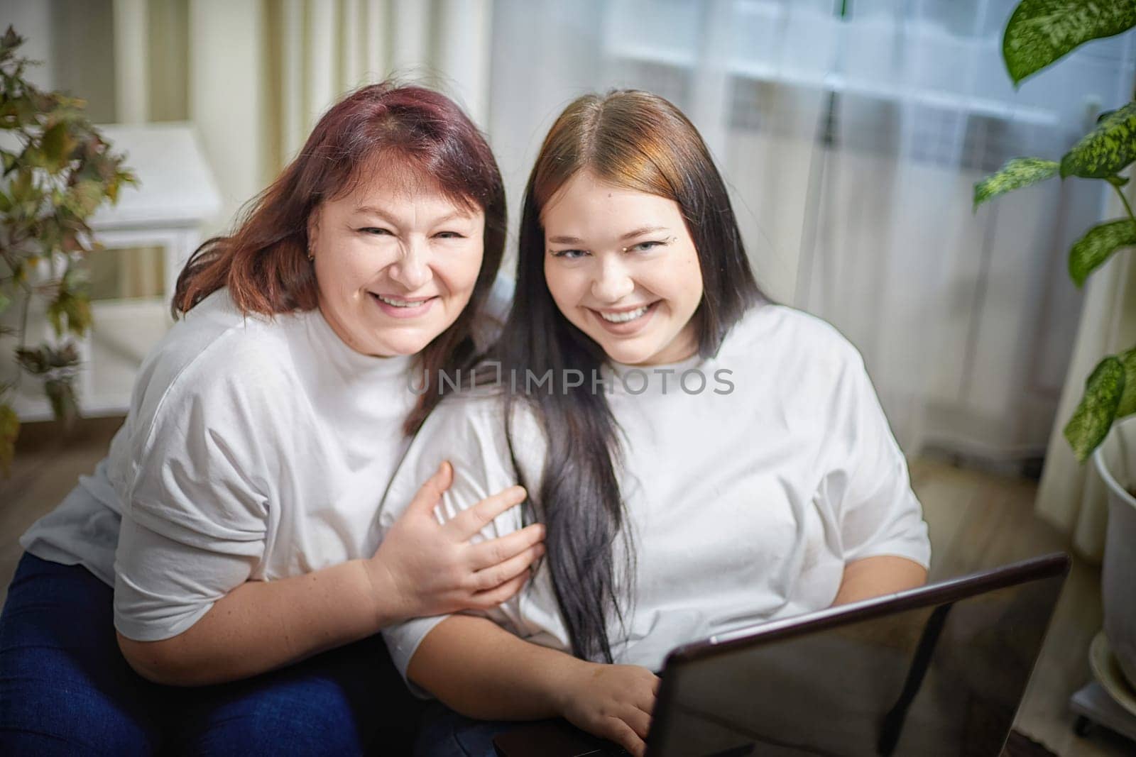Fat funny funny adult mother and daughter with laptop indoors. A teenage girl teaches a middle-aged woman modern technology. Internet, chatting