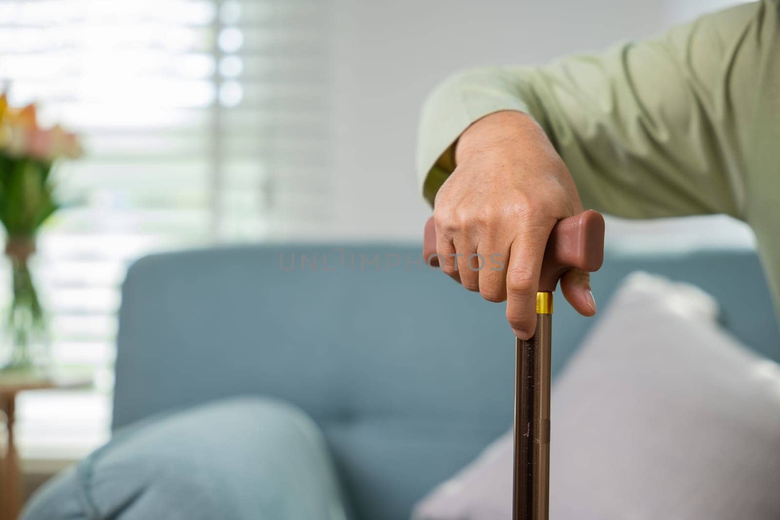Asian senior old man with eyeglasses type to standing up from sofa with walking cane stick to walk at home, Elderly suffering from knee pain ache holding handle of cane, retirement medical healthcare