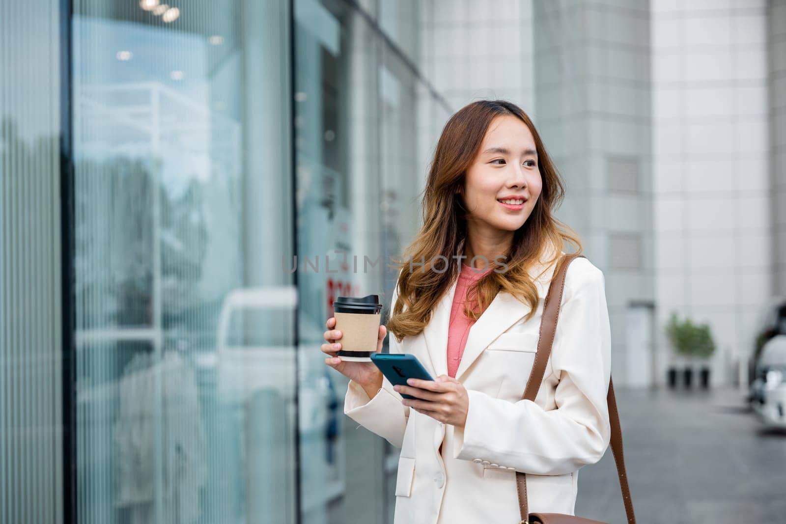 Busy businesswoman juggling coffee and cell phone, staying connected while walking to work in the morning.