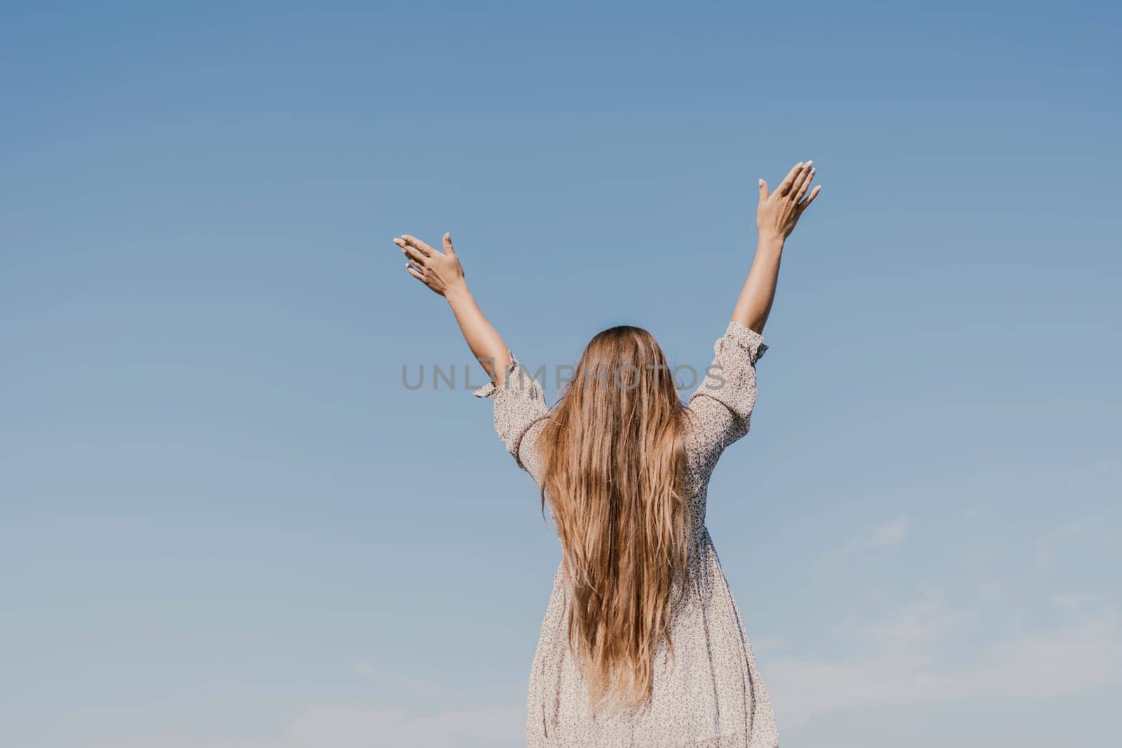 A woman with long hair is standing on the beach, looking up at the sky. She is wearing a dress and she is happy