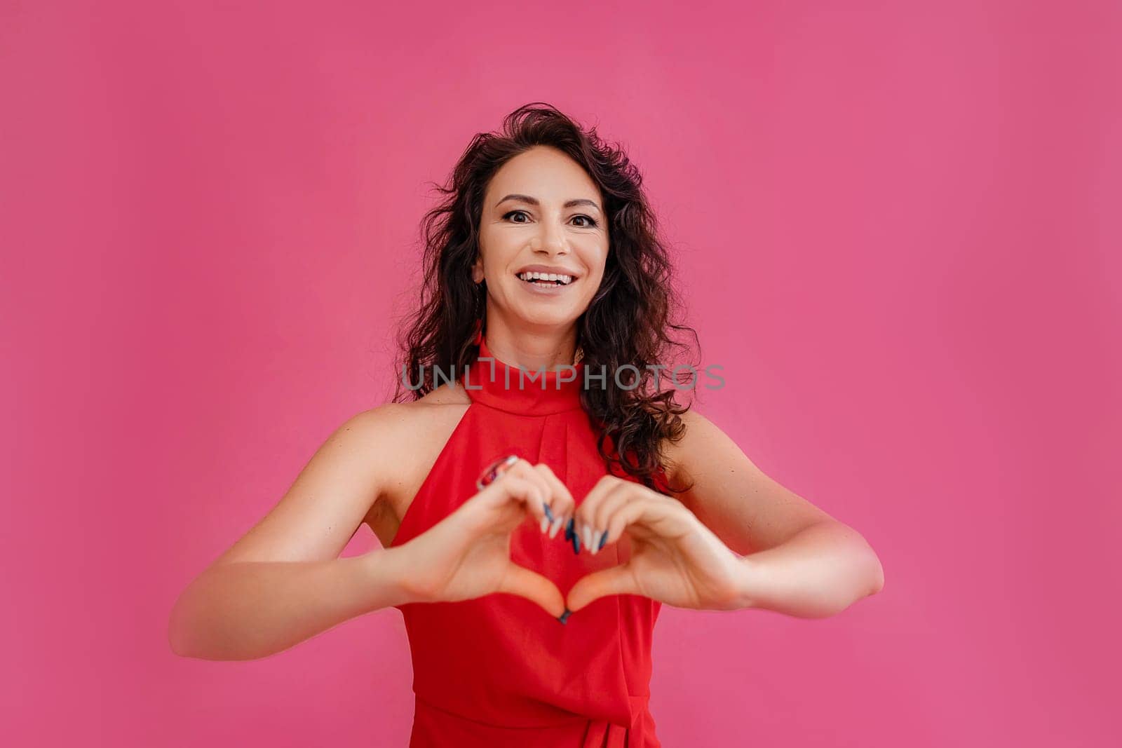 A woman in a red dress is smiling and holding her hands together to make a heart shape. Concept of love and happiness