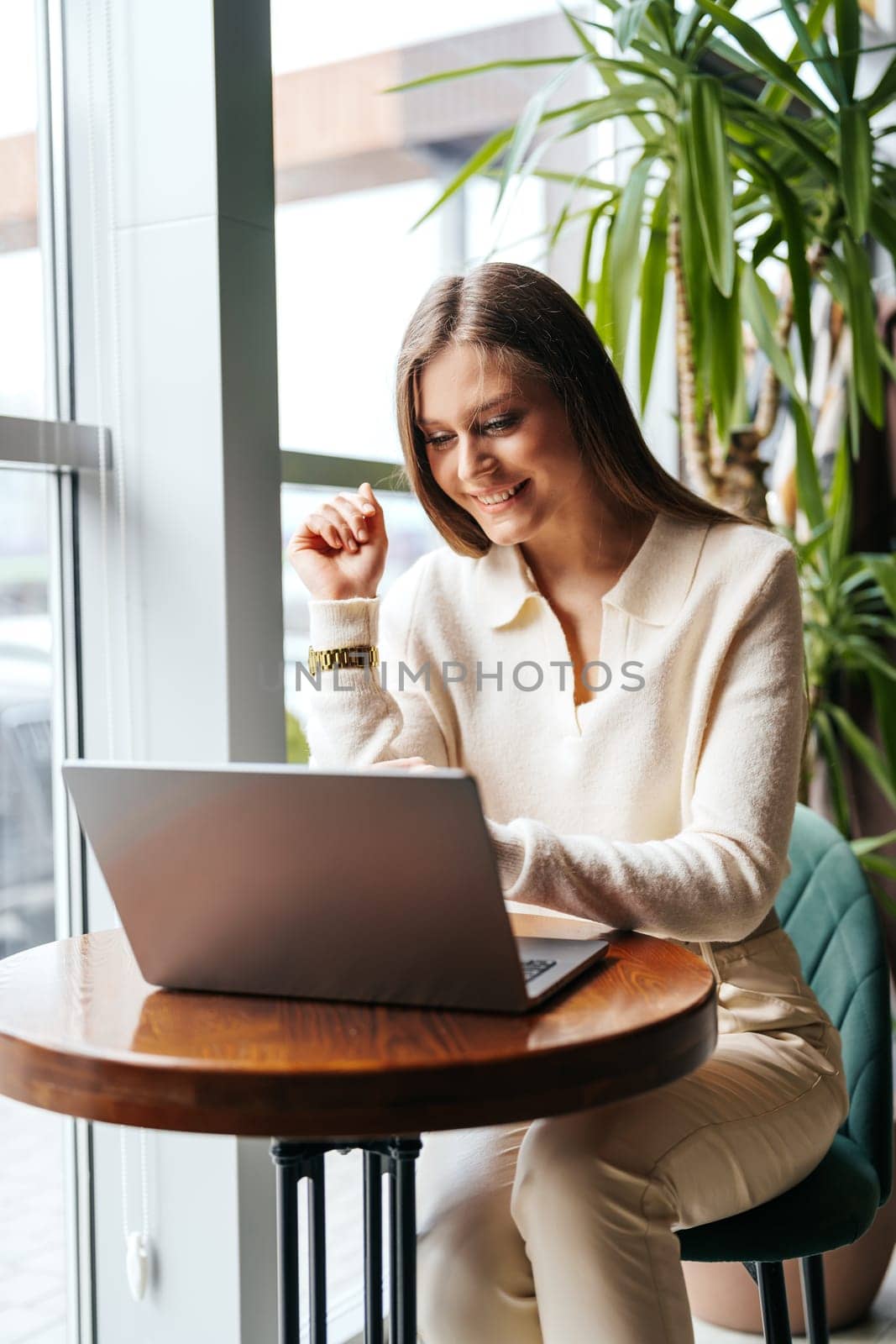 A woman is seated at a table, focused on using a laptop computer. She is typing and viewing the screen intently, possibly working or studying.