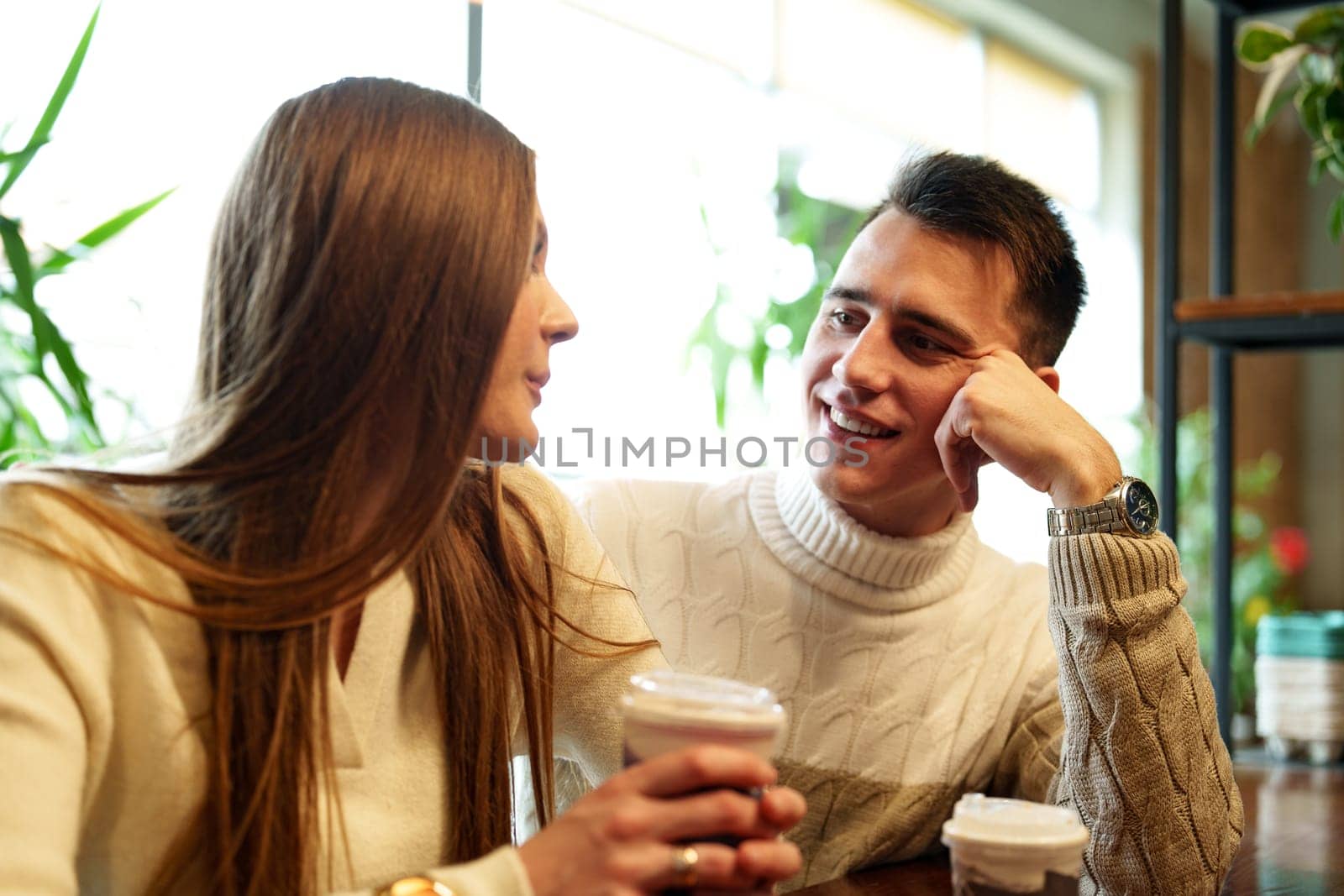 Smiling Couple Enjoying Warm Beverages at a Cozy Cafe on a Sunny Afternoon by Fabrikasimf
