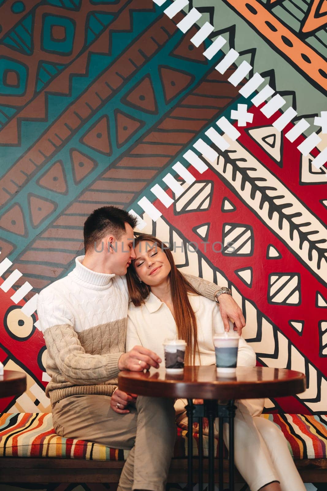 A Man and Woman Sitting at a Table in Front of a Colorful Wall by Fabrikasimf