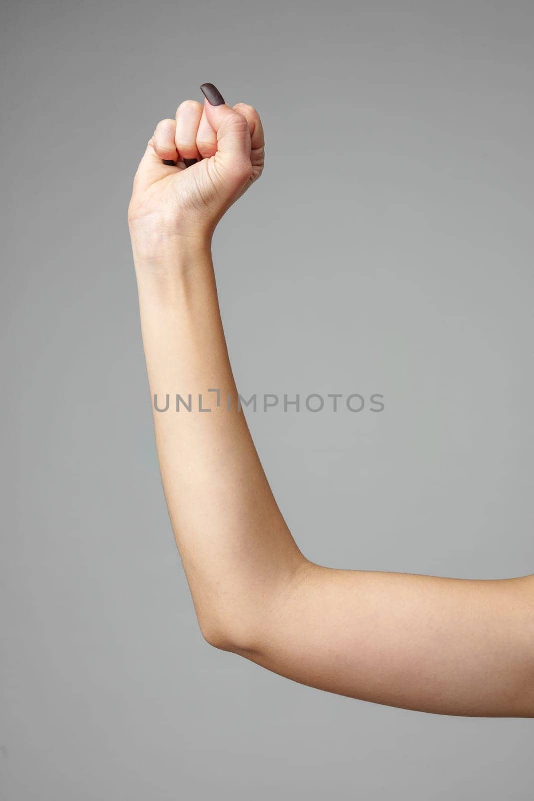 A single human arm is raised in a clenched fist, symbolizing determination, strength, and unity. The arm is displayed against a neutral gray backdrop, highlighting the muscular form and skin texture. The focused composition emphasizes the power of human expression through gesture.