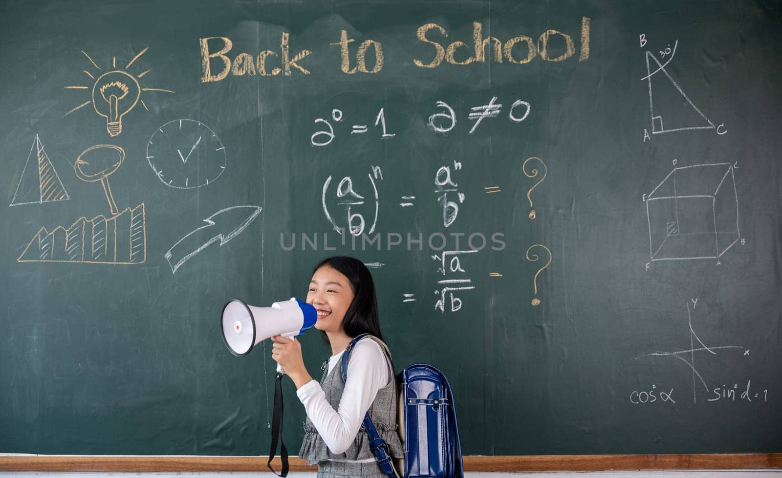 A girl is standing in front of a chalkboard with the words Back to School written on it. She is holding a megaphone and smiling