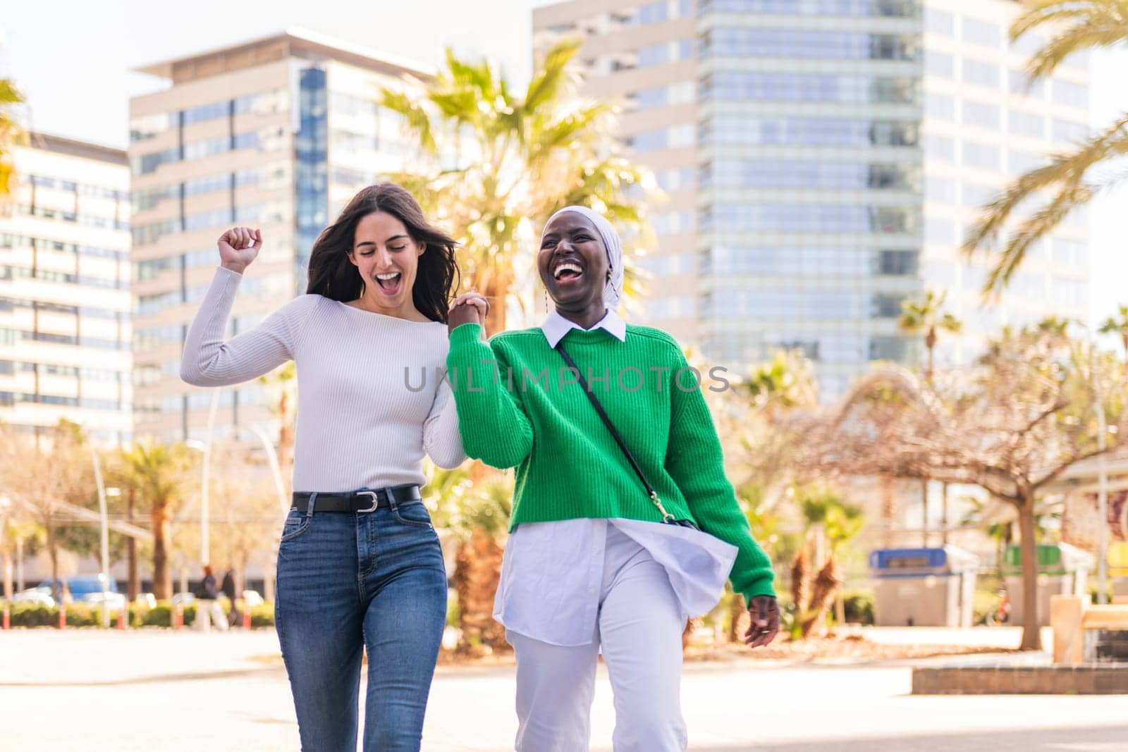 young multiracial couple of two women walking laughing happy through the city holding hands, concept of diversity and modern lifestyle, copy space for text
