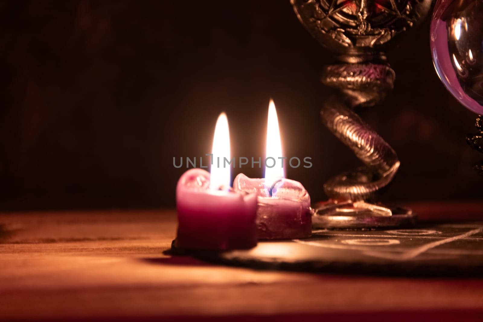 A detailed close-up shot of two lit pink candles with a dark, mystical background, emphasizing a ritualistic theme