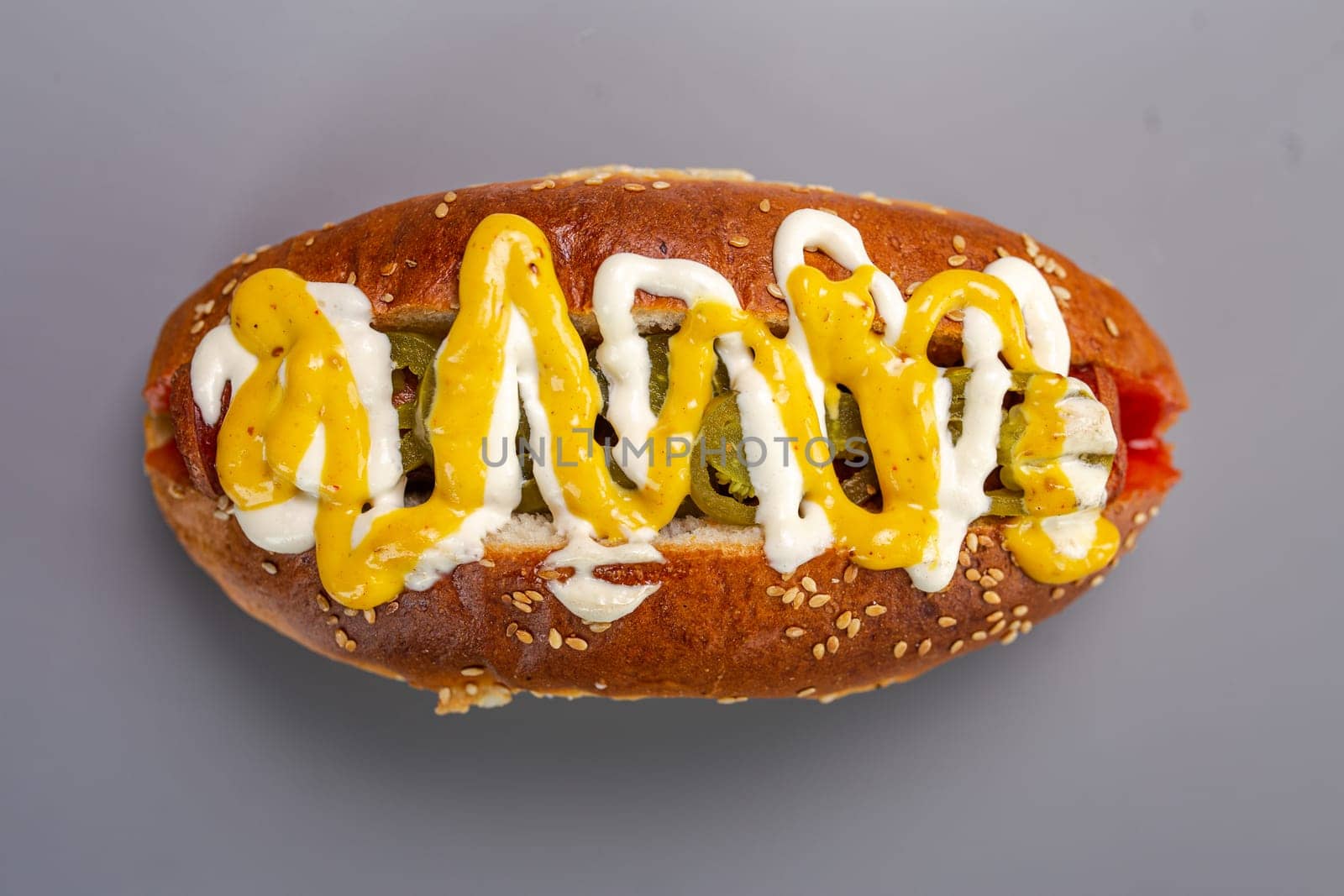 Hot dog sausage in a bun with sauces, isolated on a gray background.