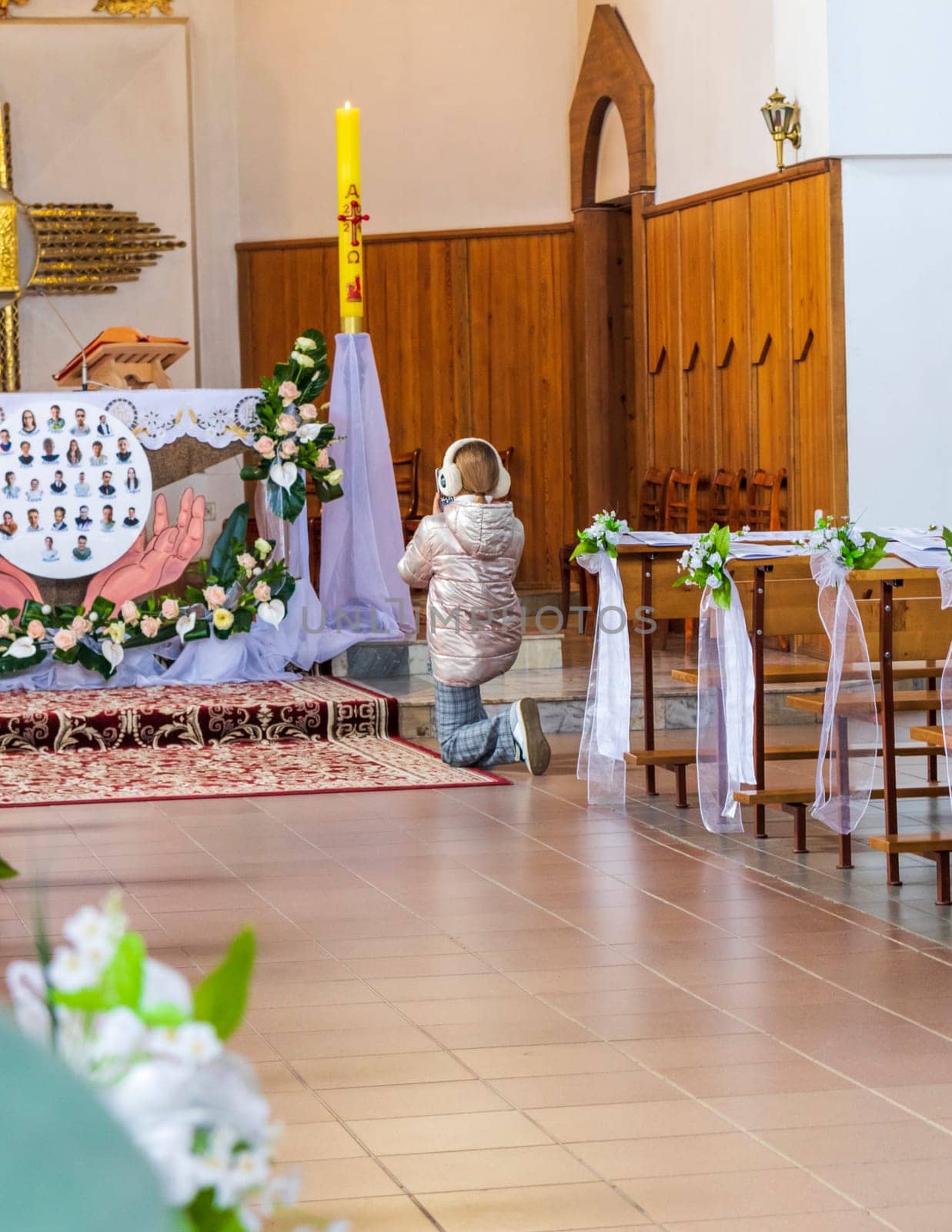 Shot of girl, wearing headphones, kneeling at the altar at Roman catholic church, says prayer and taking pictures of the altar