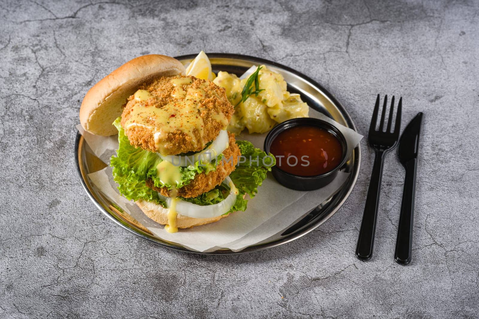 Double fish burger with potato salad on a metal plate