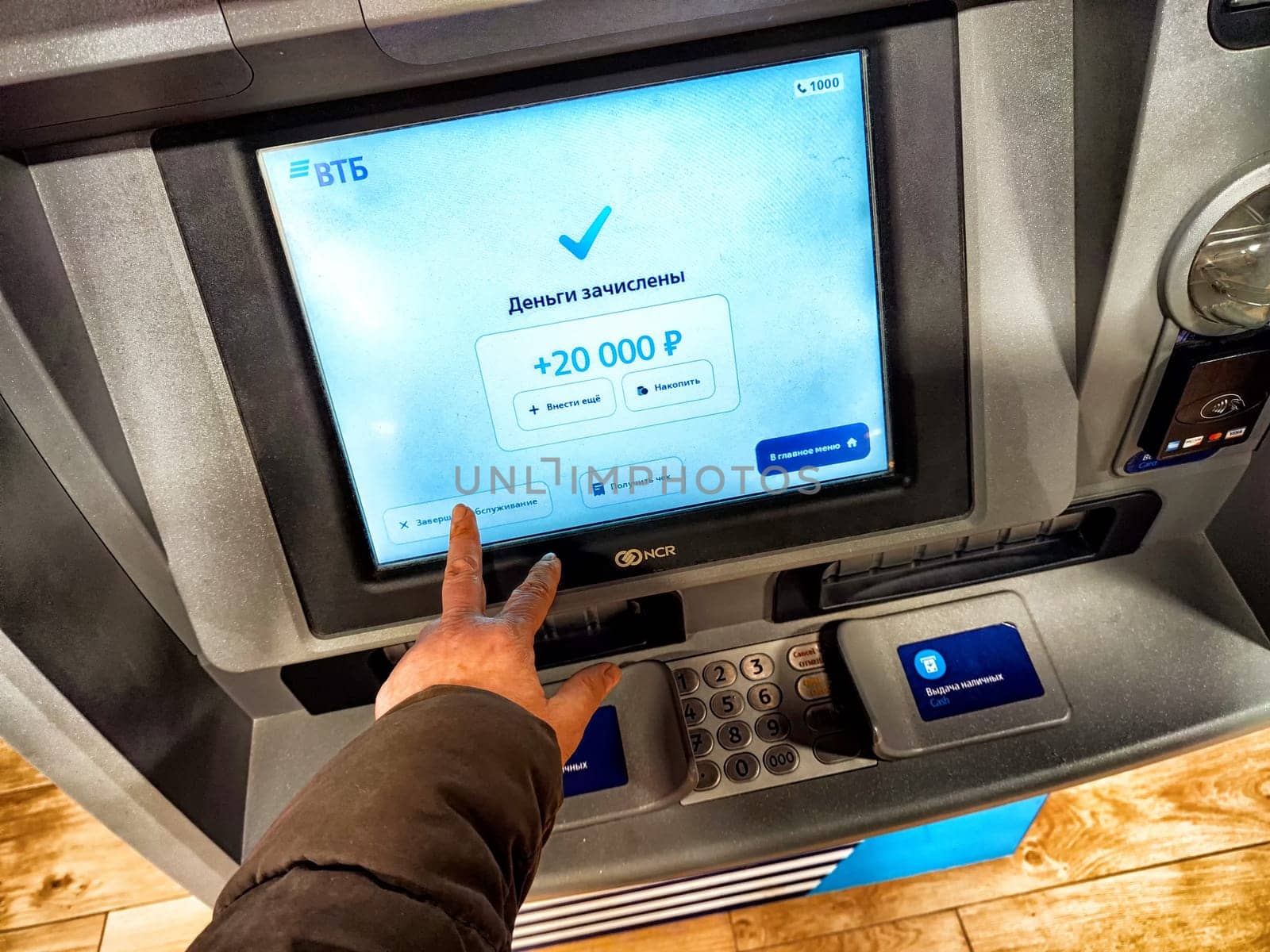 Kirov, Russia - April 28, 2024: Person Withdrawing Cash From ATM in Russia. Hand pressing button on an ATM with a Russian language screen