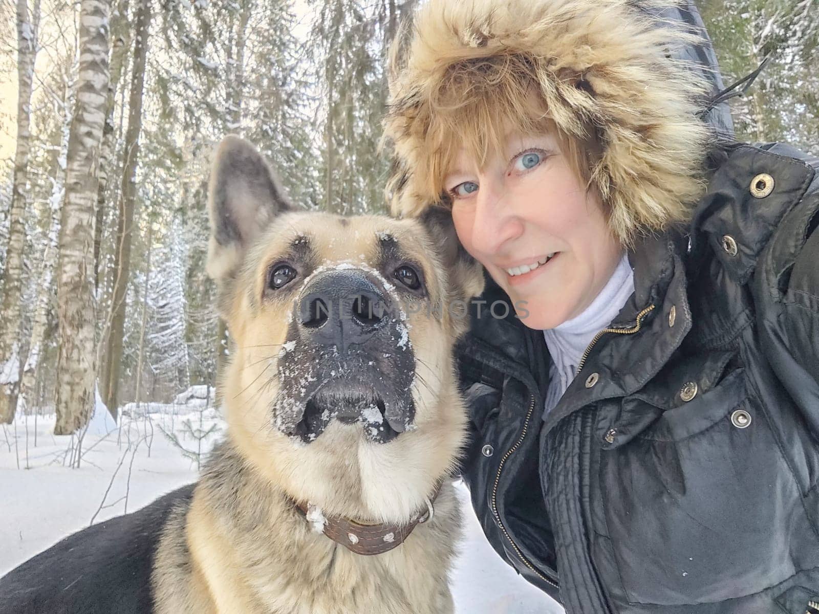 Adult girl with shepherd dog taking selfies in winter forest. Middle aged woman and big shepherd dog on nature in cold day. Friendship, love, communication, fun, hugs