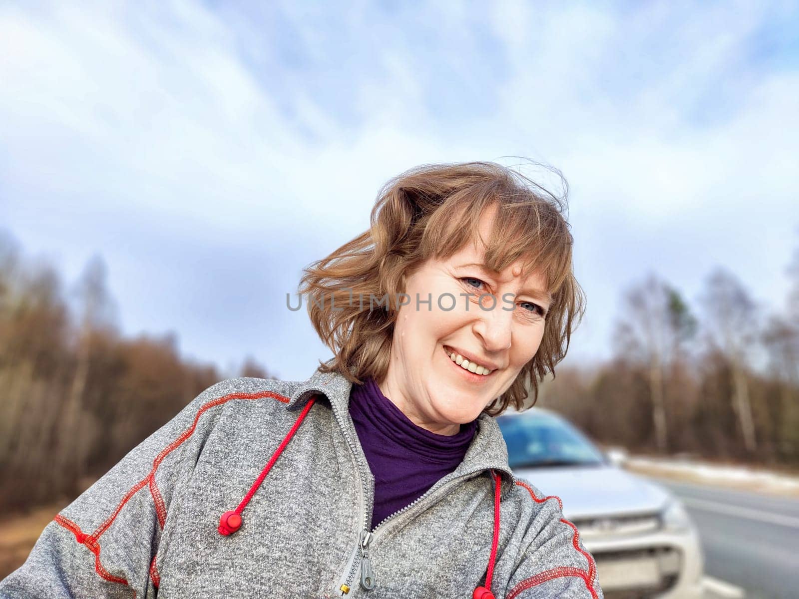 A woman takes a selfie on the road near a car. The concept of car travel. A woman captures a selfie with her car in the background during a road trip by keleny