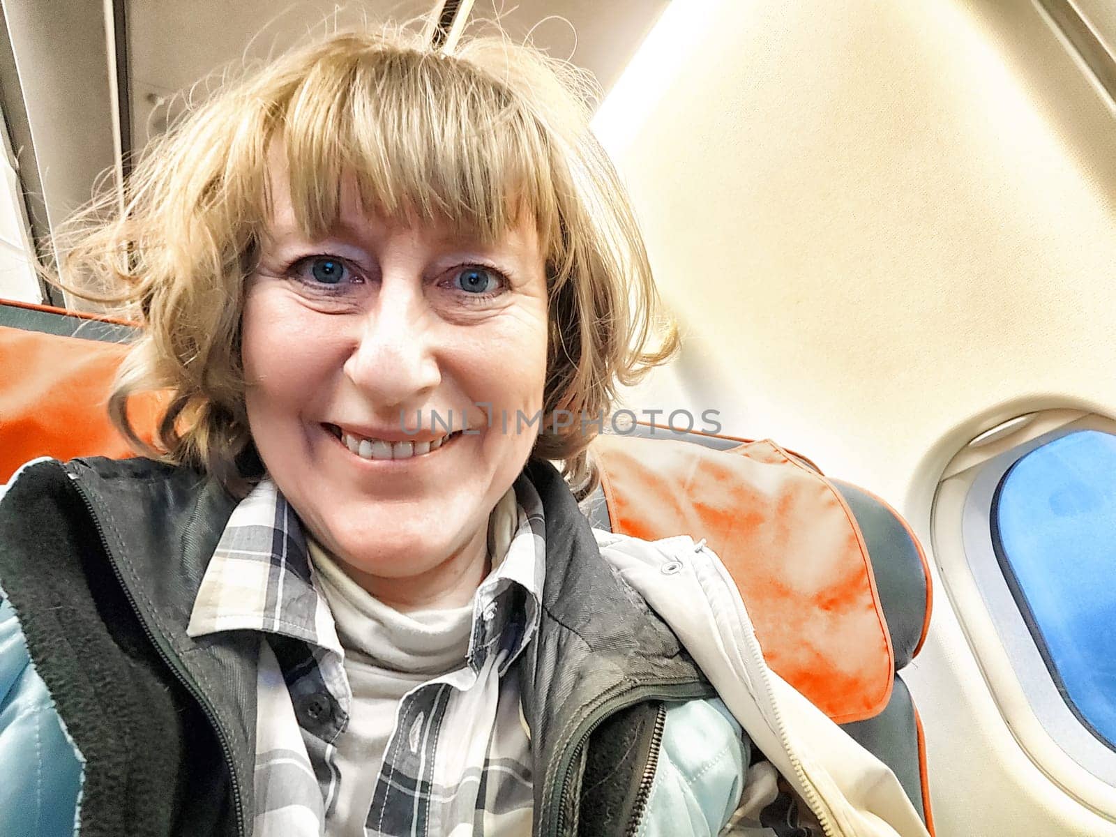 A middle-aged woman takes a selfie on a plane. Portrait of a girl. Smiling Woman on Airplane by keleny