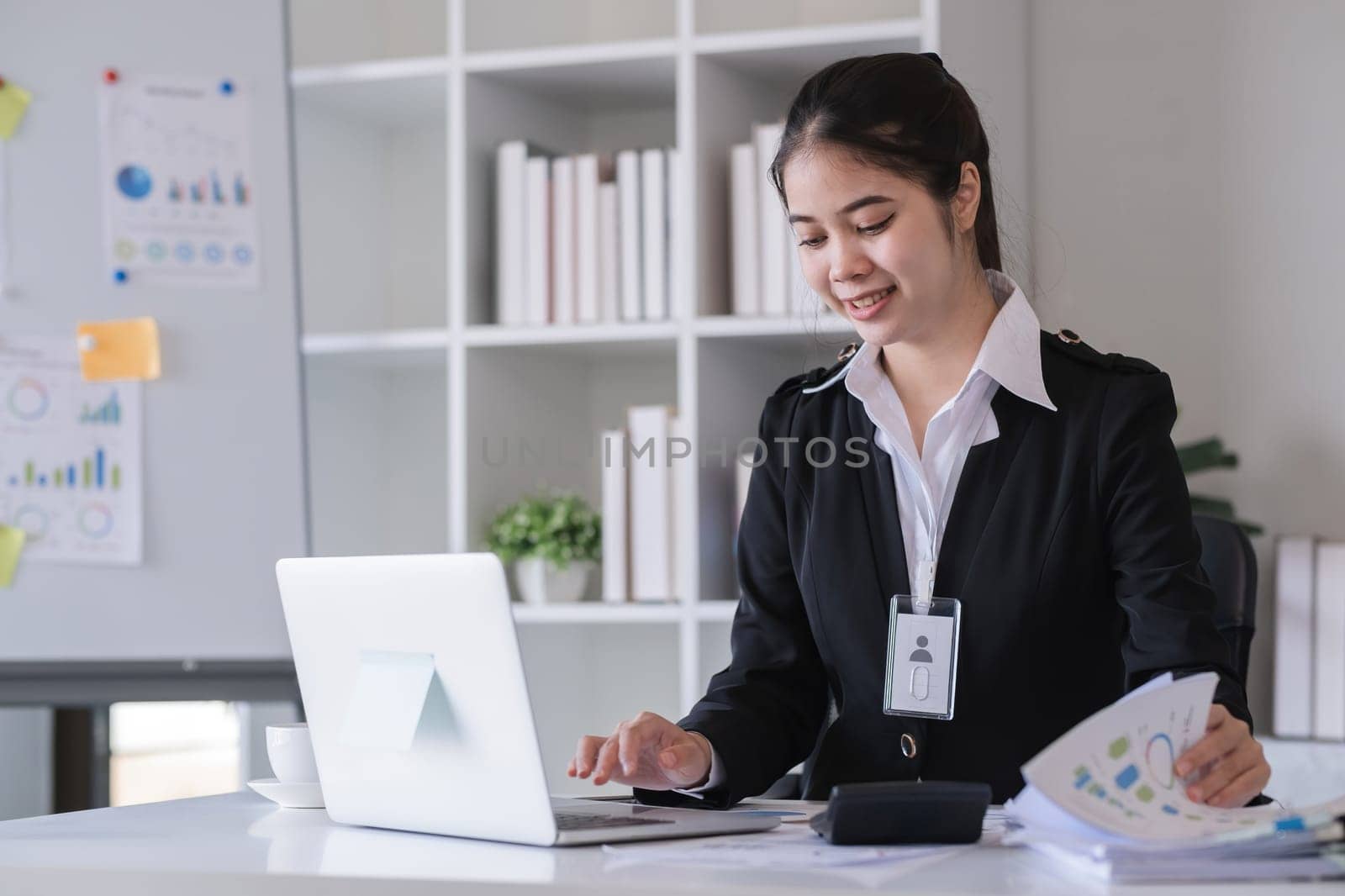 Accountant sitting with financial documents, using laptop, calculating financial and tax figures for company on table in office by wichayada