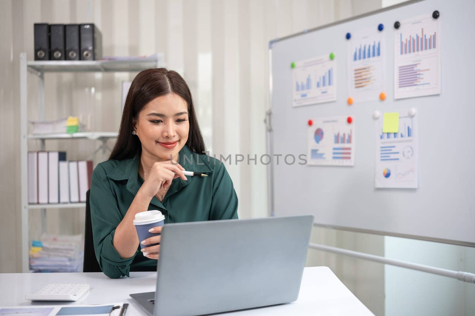 Asian businesswoman working on financial document with laptop on desk in office room by wichayada