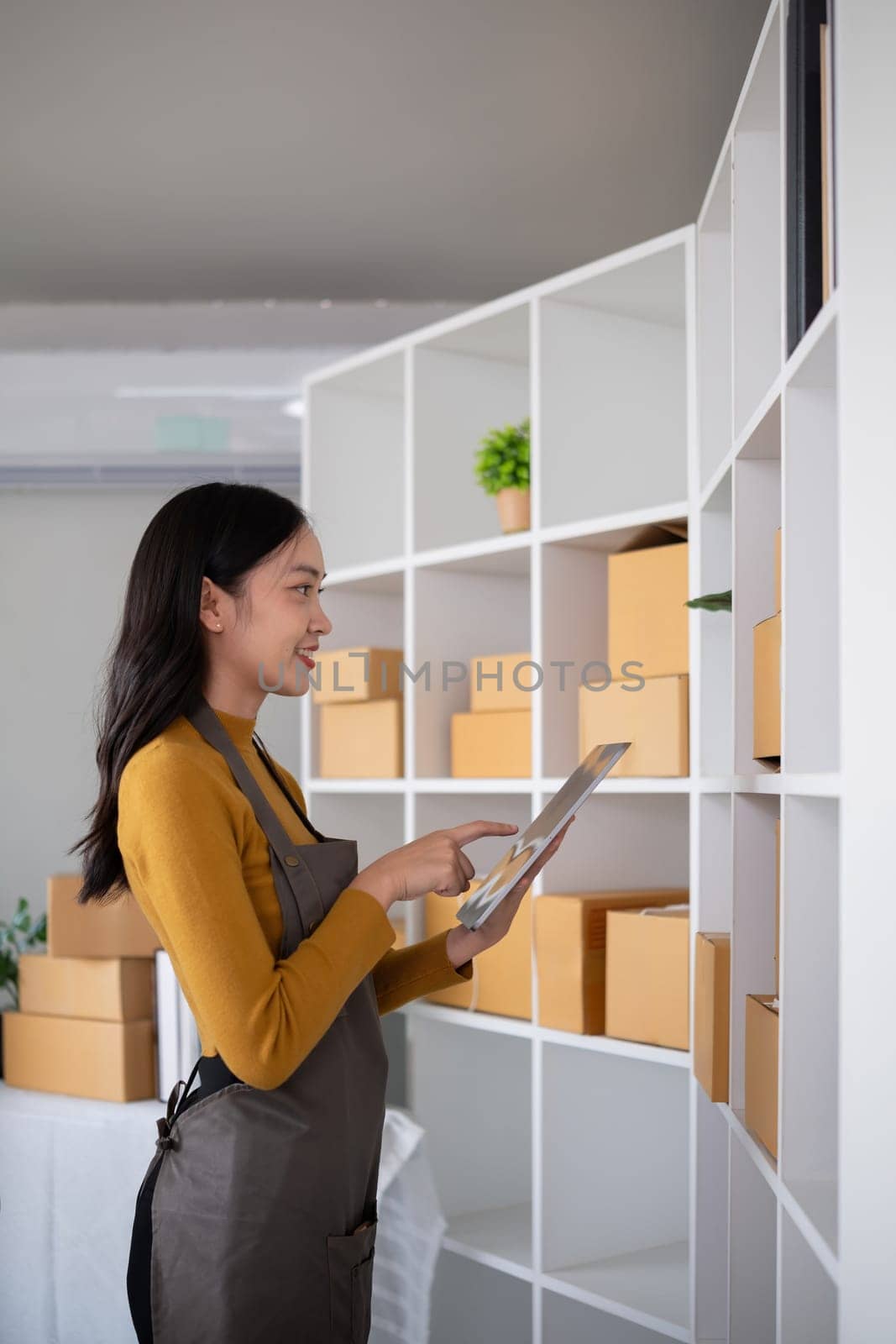 Young woman working in warehouse with packages using tablet for inventory management.