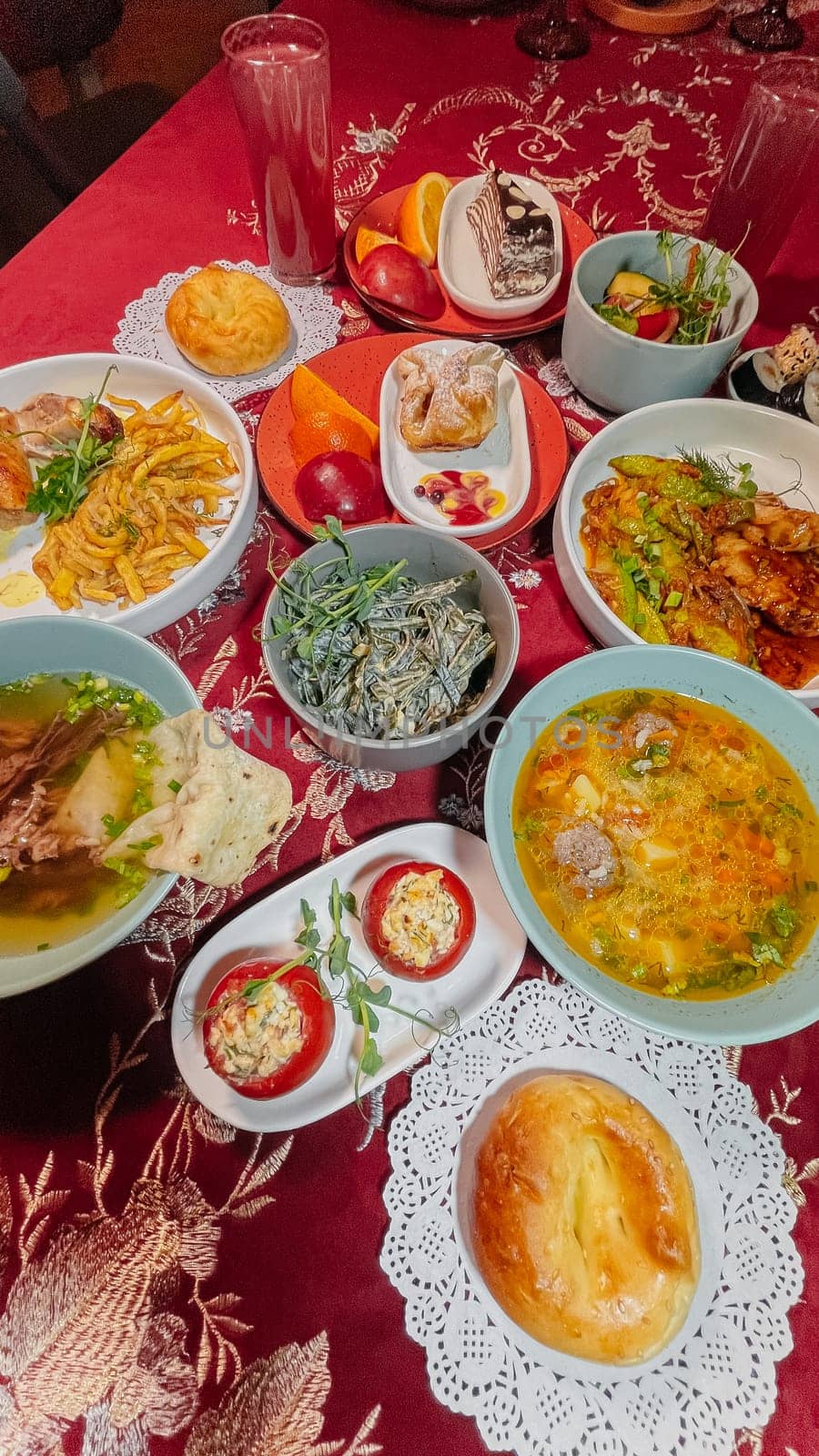 Top view of Uzbek traditional dishes on a table with red tablecloth. Soups, salads, main courses, pastries, drinks.