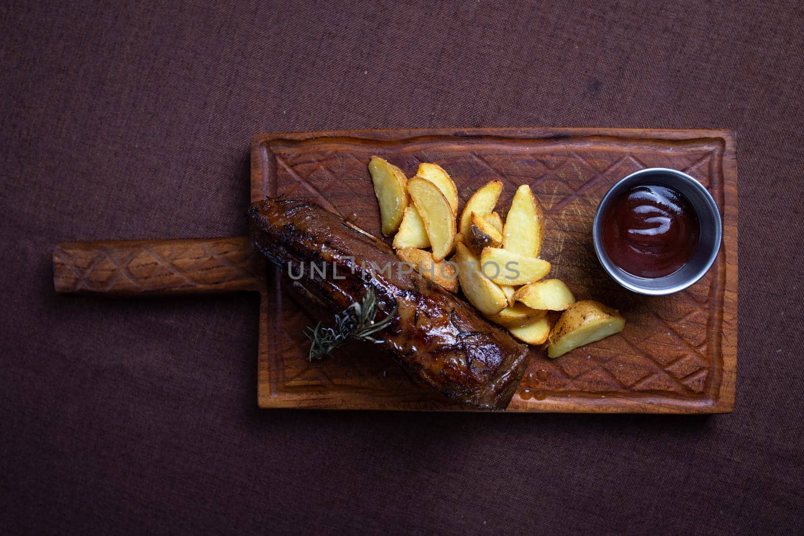 top view of the Beef steak with baked potato wedges and rosemary on a wooden board by Pukhovskiy