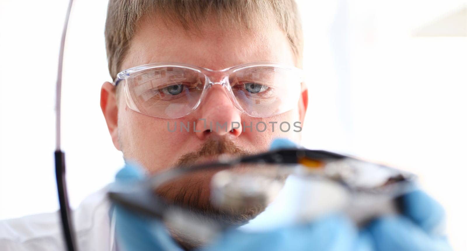 A male repairman wearing blue gloves is holding a hard drive from computer or laptop in hands. Performs fault diagnostics and performs urgent repairs recovery of lost data during deletion HDD closeup