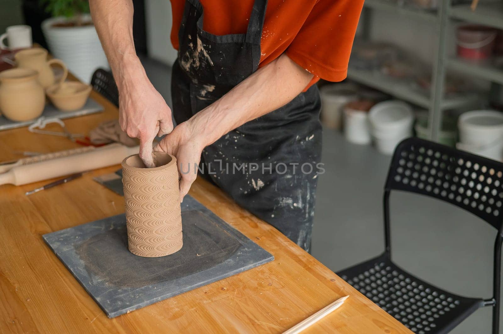 Close-up of a man's hands making a patterned cylinder out of clay