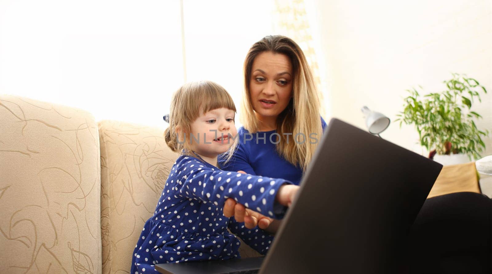 Cute little girl on couch with mom use laptop pc for chat with her dad away on business portrait. Point finger hand in display social web network bank mortgage credit wireless ip telephony concept