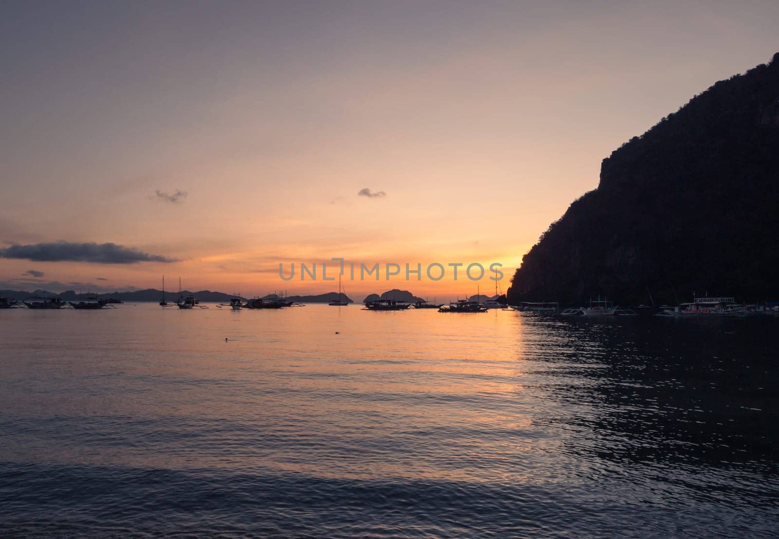 Boats anchored in a calm bay at sunset near scenic islands. Philippines, Palawan. by Busker